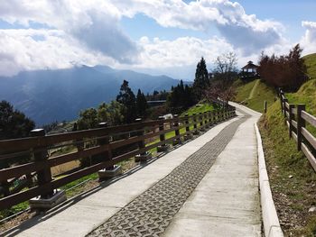 Empty footpath leading towards mountains against sky