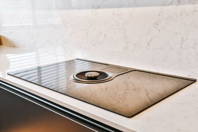 Modern black induction stove with integrated round extractor hood on white marble counter placed at wall light kitchen at home