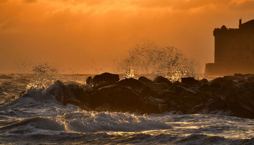 Scenic view of sea with waves against sky during sunset