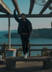 Portrait of young man standing on railing against sea