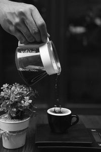 Cropped hand of person pouring coffee in cup on table