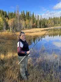 A full body portrait of woman fishing in a lake on an autumn day.