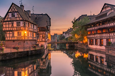 River by illuminated buildings against sky at sunset