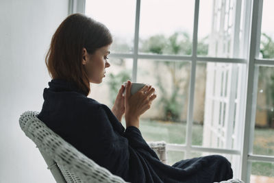 Woman looking at camera while sitting on window