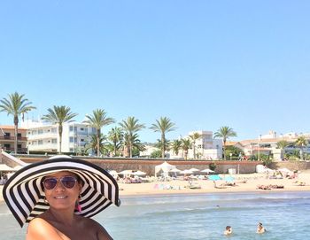 Young woman wearing striped hat by sea against clear sky