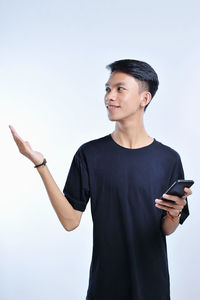 Young asian student man holding a smart phone and open hand palm aside, presenting to copyspace