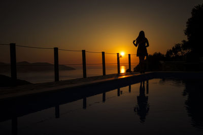 Silhouette people standing on shore against sky during sunset