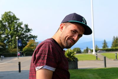 Portrait of confident man wearing baseball cap on field against sky