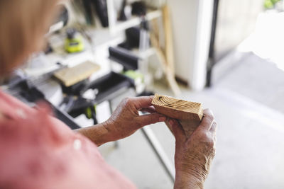 Cropped image of senior woman holding wooden plank in workshop