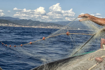 Fisherman's hand lowering the nets in the mediterranean sea, in the background the italian coast

