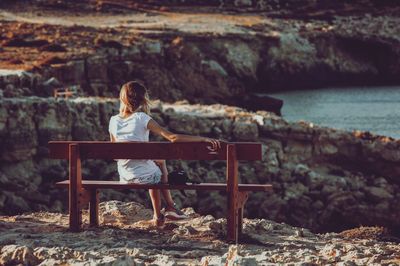 Rear view of man sitting on bench by sea