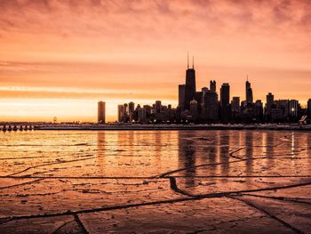 Sea by cityscape against sky during sunset