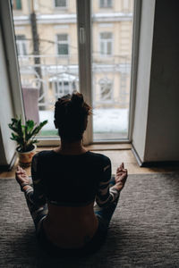 Rear view of woman sitting by window at home