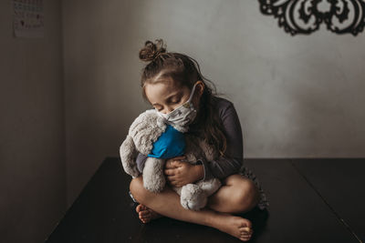 Young girl with mask on cuddling with masked stuffed animal