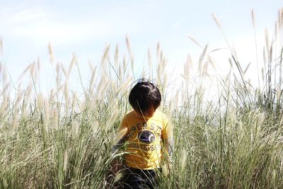 Boy standing amidst crops in field against sky