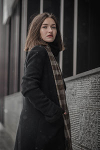 Portrait of young woman in warm clothing standing against building