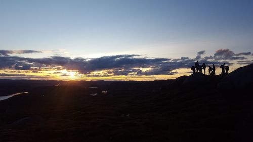 Silhouette people on land against sky during sunset