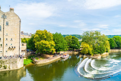 Arch bridge over river amidst trees and buildings against sky