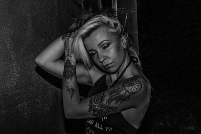 Tattooed female hipster standing against wall at night