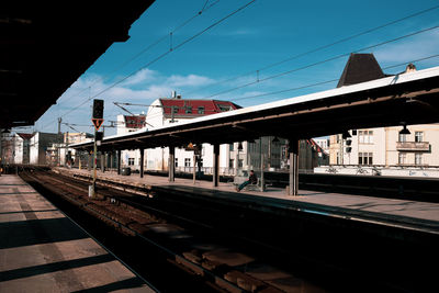 Man sitting at railroad station in city against sky