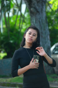 Young woman using phone while standing on tree