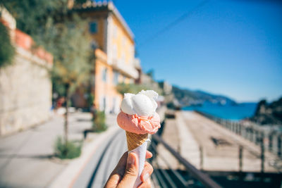 Cropped hand holding ice cream cone against clear blue sky