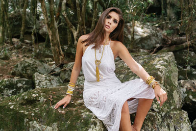 Portrait of young woman sitting on rock in forest