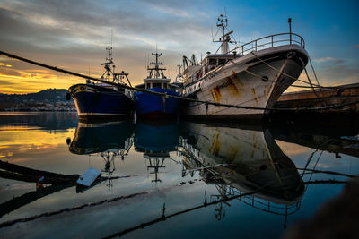 Fishing boat moored at harbor against sky during sunset