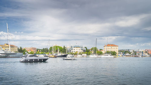 Sailboats in river by buildings against sky