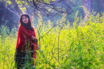 Young woman standing by tree on field