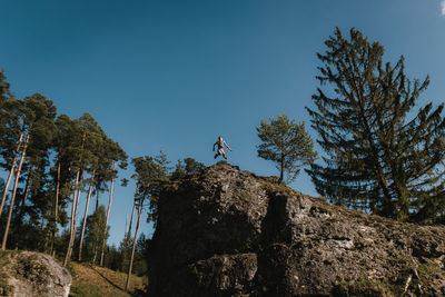 Low angle view of boy jumping over rock against clear blue sky