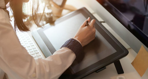 Midsection of woman using graphics tablet and digitized pen on table