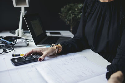 Midsection of female engineer with blueprint on desk at home office