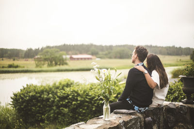 Couple looking at lake while sitting on retaining wall