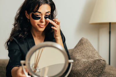 Young woman applying coal eye patch at home