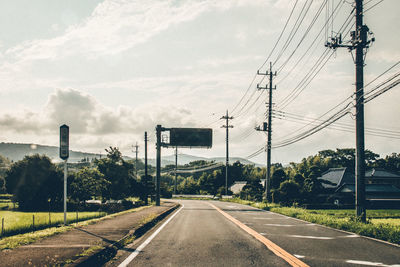 Road by electricity pylon against sky
