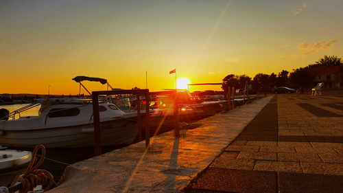 Boats moored on street by sea against sky during sunset