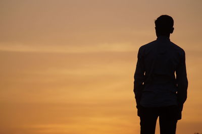 Rear view of silhouette man standing against orange sky