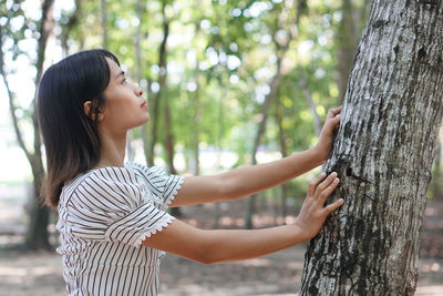 Side view of woman standing by tree trunk