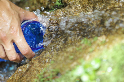 Cropped hand filling water in bottle at forest