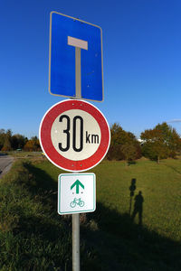 Road sign on field against clear blue sky