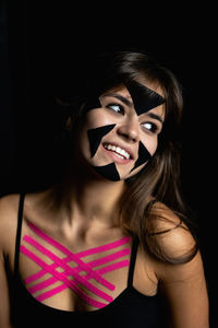 Portrait of young woman wearing mask against black background
