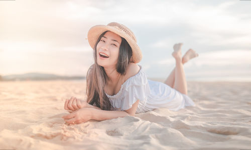 Young woman lying on sand at beach against sky