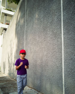 Boy running on footpath by concrete wall