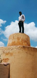 Low angle view of man standing on rock against sky