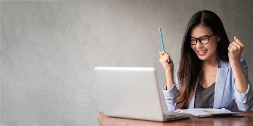 Young woman using mobile phone while sitting on wall