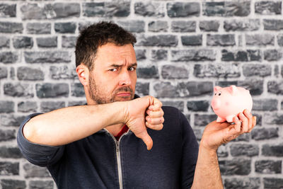 Portrait of man holding piggy back and gesturing against brick wall