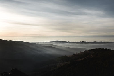 Scenic view of silhouettes mountains against cloudy sky at sunset