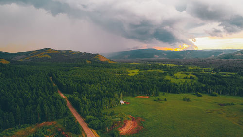 Scenic view of trees on field against cloudy sky during sunset