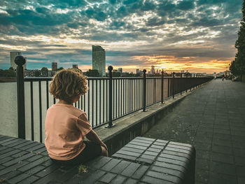 Rear view of woman sitting on railing against sky